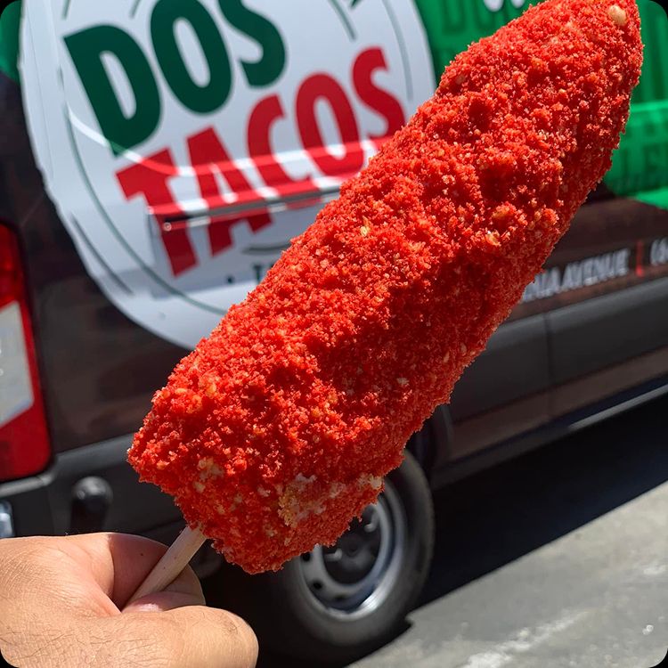 Close up of a customer holding a Flamin' Hot Cheeto elote in front of the Dos Tacos truck.